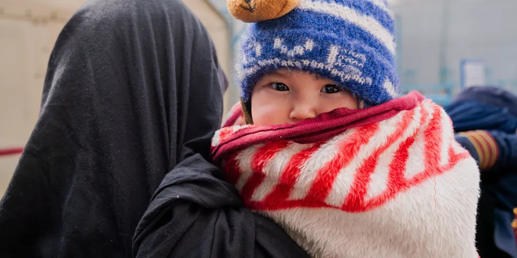 A mother holds her 1 year old son while waiting for aid at a UNHCR distribution centre in Afghanistan