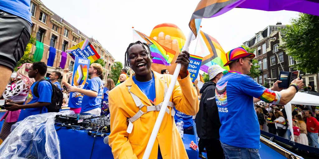 LGBTIQ+ refugees wave pride flags and hold up signs during a pride march in Amsterdam, The Netherlands