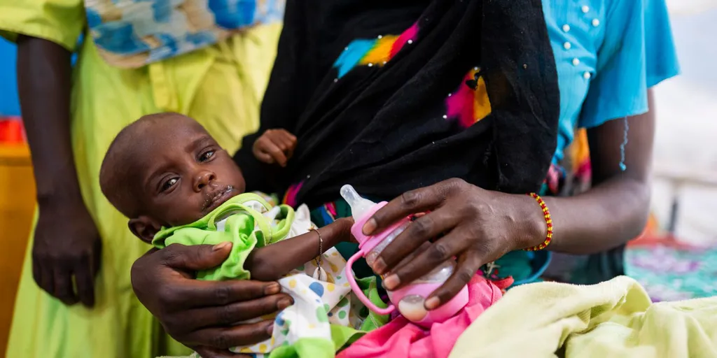 Baby held in a woman’s arms while she feeds the infant with a bottle of milk